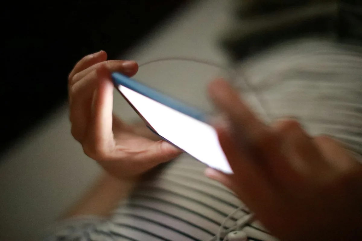 暗い部屋で、両手に持ったスマートフォンの画面が光っている