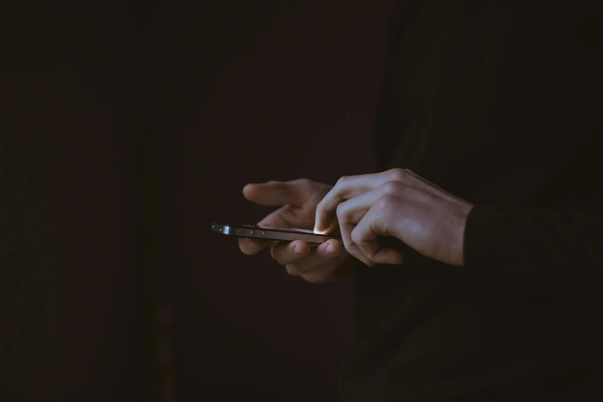 暗がりの中でスマートフォンを両手で持ち、家族に連絡しようとしている手元