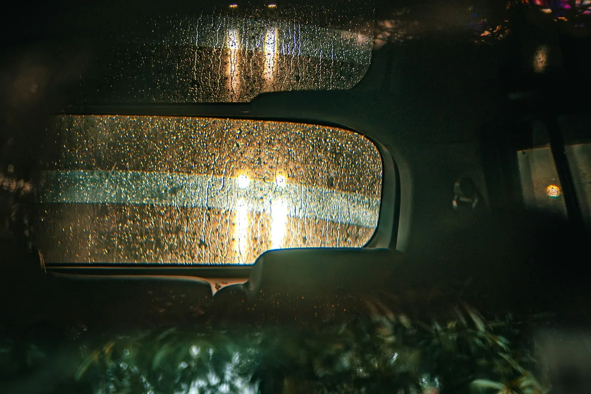 雨粒のついた車の窓越しに、夜の明かりがにじんで見える車内の情景